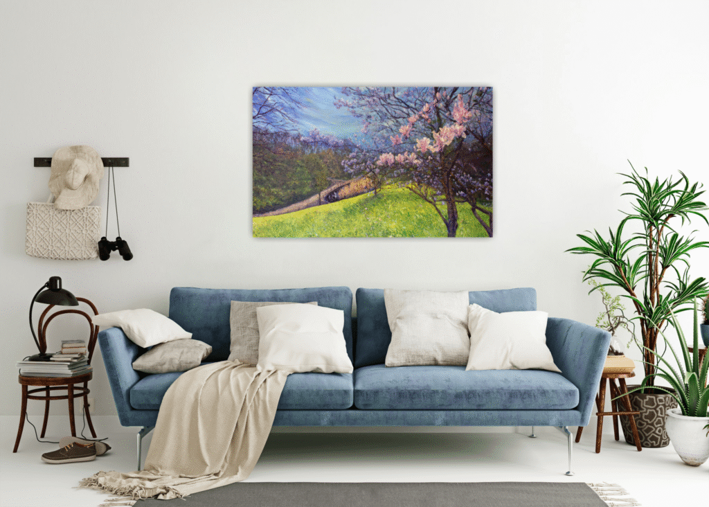 View of large painting featuring a magnolia tree in an informal room setting with blue sofa, draped blanket, large plants and assorted personal items